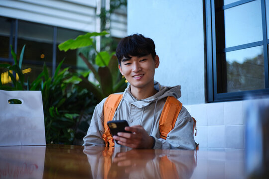 Young Asian delivery guy sitting with a food package on the table.