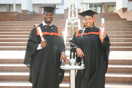 Young african man and woman graduating college, wearing a graduation gown cap