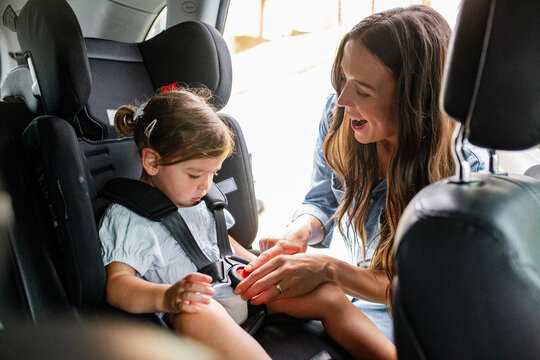 Mother fastening seatbelt on toddler daughters car seat.