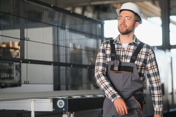 Smiling and happy employee. Portrait of industrial worker indoors in factory. Young technician with...