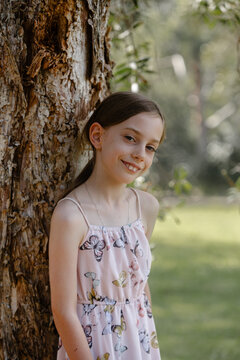 Happy girl standing beside the tree trunk outdoors