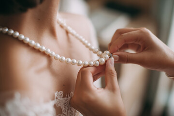 Bride prepares for wedding ceremony while adjusting pearl necklace in elegant attire in bright indoor setting