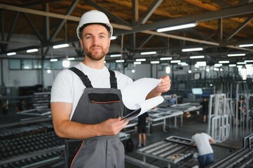 A young male engineer inspects the production of plastic window frames