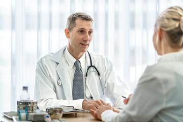Senior male doctor and female patient discussing in detailed about health concerns and possible treatment plans at hospital. Medicine and health care concept