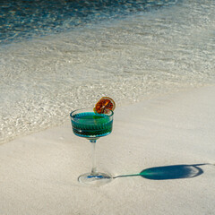 A clear, blue-toned cocktail, with a dried blood orange slice on the rim of the glass as a...