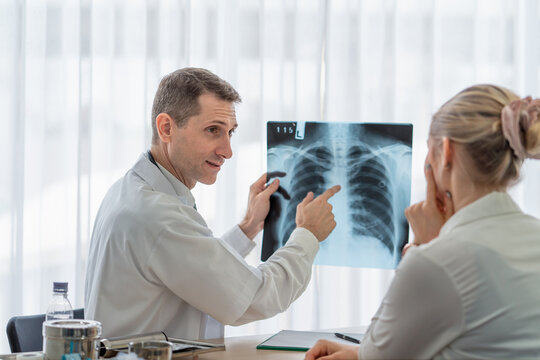 Senior male doctor explains results of chest X-ray to female patient during a medical consultation at hospital. Professional healthcare setting focused on diagnosis and patient communication.