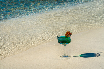 A clear, blue-toned cocktail, with a dried blood orange slice on the rim of the glass as a...