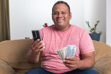 A man in a red shirt is sitting on a couch holding a cell phone
