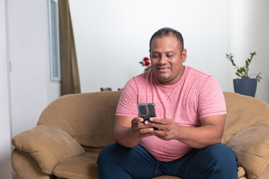 A man is sitting on a couch and looking at his cell phone - Powered by Adobe