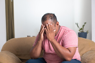 A man in a red shirt is sitting on a couch and looking down