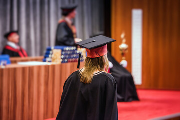 Graduation ceremony scene: back view of a female graduate walking on stage to receive her diploma....