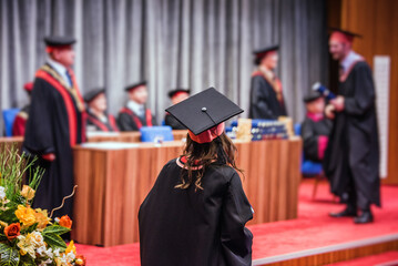Back view of a female graduate walking on stage to receive her diploma during a graduation...