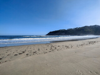 Waves crashing on sandy beach with cliff in background