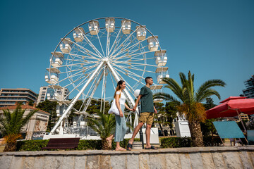 Fototapeta premium Couple Holding Hands Walking by the Ferris Wheel on a Summer Day