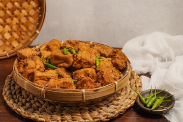 Rustic scene of Tahu on round woven mat, paired with green chili on the side.