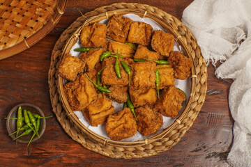 Golden fried Tahu Sumedang served on a woven bamboo plate with fresh green chili, traditional Indonesian snack.
