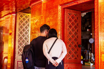 Couple exploring intricately designed interior with vibrant red walls and ornate patterns,...