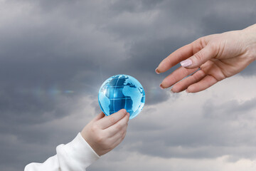 Hands passing a globe in cloudy atmosphere.