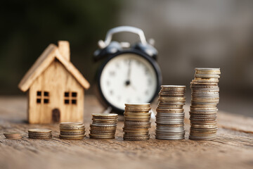 Stack of coins growing in size next to a wooden house model and a clock, symbolizing long-term savings and retirement planning, with copy space for economic concept