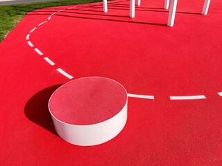 A station on a red fitness trail. The red floor with white markings is elastic.