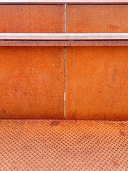 Background: Detail of a wall composed of rusty steel sheets. The floor is made of rusty steel checker plate.