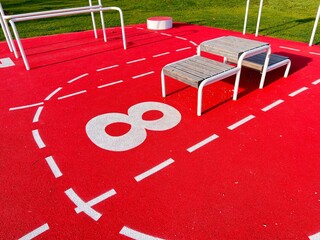 A station numbered eight on a red fitness trail. The red floor with white markings is elastic.