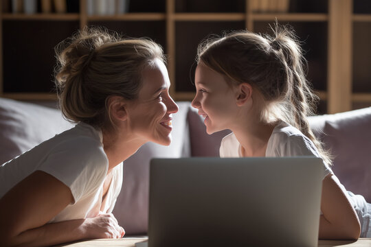 Happy mother and daughter smiling together during online school session at home with laptop