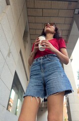 Low angle view of confident young woman with coffee and urban streetwear look