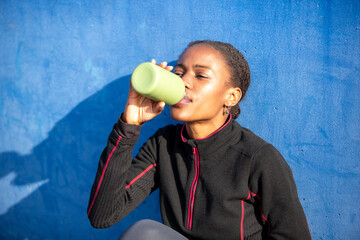 Sporty African woman hydrating with green bottle after workout