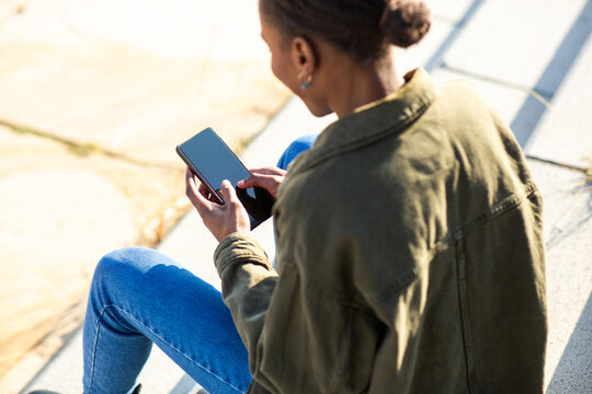 Mixed race woman using smartphone while sitting on outdoor steps