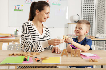 Cute boy learning letters with teacher at desk in school