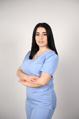 A beautiful, smiling female nurse in a blue medical suit on a white background. Portrait of a young nurse. The image conveys professionalism, confidence and experience in the field of healthcare