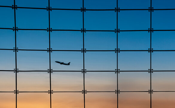 Silhouette of an airplane against a window with square grids and a sunset n the background