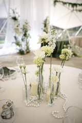 Wedding venue table elegantly set with white flower centerpiece in glass vases. Pearls and candles...