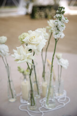 Wedding venue table elegantly set with white flower centerpiece in glass vases. Pearls and candles add an enchanting touch, creating an inviting and sophisticated atmosphere.