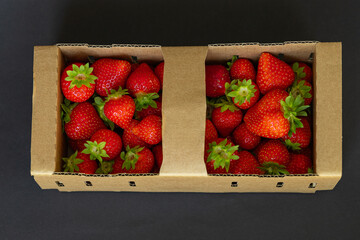 Fresh ripe strawberries in eco cardboard container on black background. Healthy seasonal eating,...