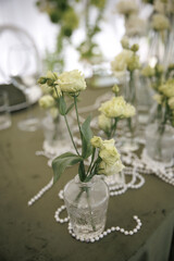 Elegant table setting featuring tall white roses and delicate flowers in glass vases, intertwined with pearl strands on a dark cloth, creating a sophisticated atmosphere.