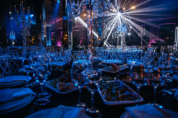 Luxurious banquet hall with crystal chandeliers and meticulous table settings under blue lighting....