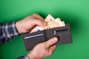 Man taking euro banknotes from wallet on green background. A man pulls euro bills out of a black...