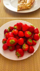 Fresh strawberries resting on a white plate beside a slice of apple pie