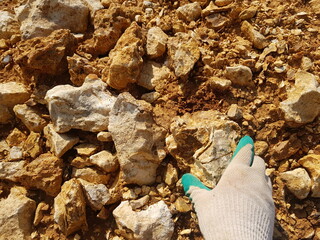 Hand in work gloves picking up a rock, inspection of geological rocks on quarry dumps