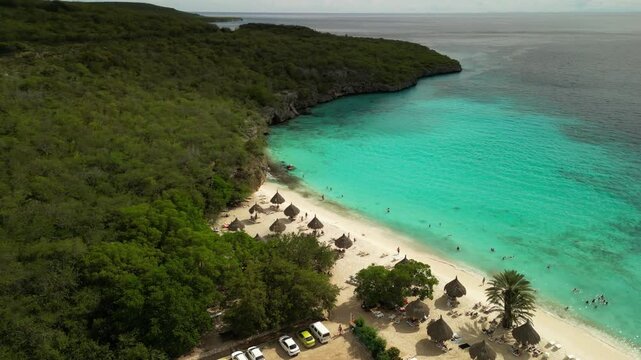 Top-down drone shot of beachgoers in crystal-clear shallows, coral patches visible below. Best for ocean-themed travel footage. Filmed 21 June 2025, Curacao, Cas Abao beach
