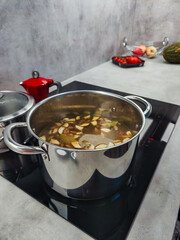 Chef preparing broth with vegetables in stainless steel pot on induction stove Mushroom soup