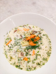 Creamy mushroom soup with dill and vegetables in white bowl