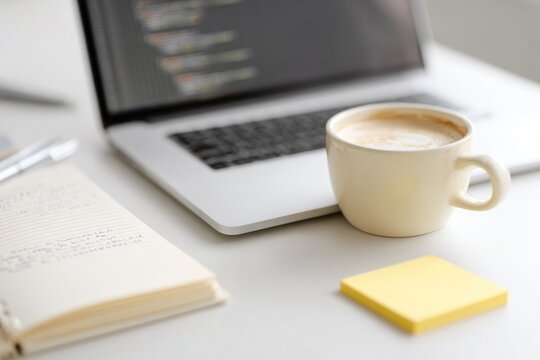 flat-lay of laptop keyboard javascript book coffee cup and sticky notes with code snippets on white desk
