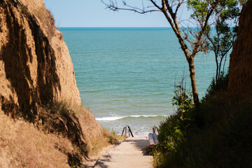 Scenic view of a narrow path between cliffs leading down to a calm sea, with stairs and railings...