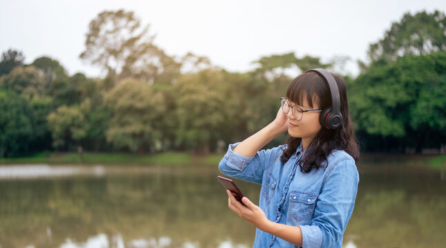 Woman relaxing with headphones and phone by a tranquil lake.