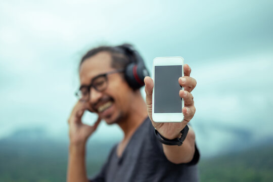 Smiling man in headphones showing a smartphone screen.