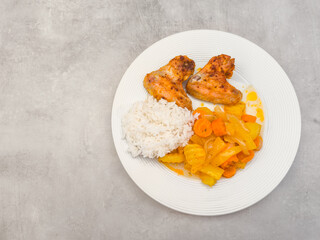 Roasted chicken wings with rice and stewed vegetables on white plate, copy space