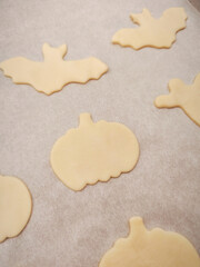 Halloween cookies waiting on baking paper, raw dough shapes of pumpkins, bats, and ghosts ready for the oven, copy space